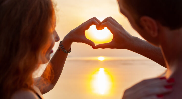 A imagem é a foto de um casal de namorados contemplando o pôr do sol.