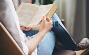 A imagem é a foto de uma mulher lendo um livro.