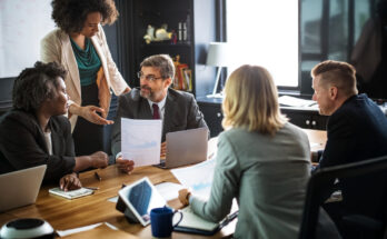 A imagem é a foto de funcionários de uma empresa juntos em uma sala de reunião.