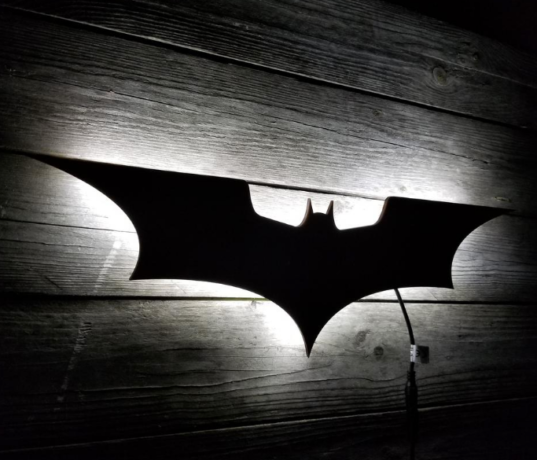 A imagem é a foto do presente entregue na saída do evento, que é uma luminária de parede, no formato do símbolo do Batman.