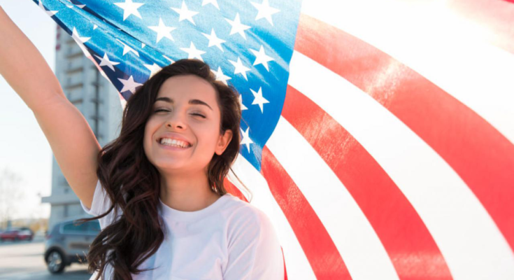 A imagem é a foto de uma jovem estudante segurando a bandeira dos Estados Unidos.